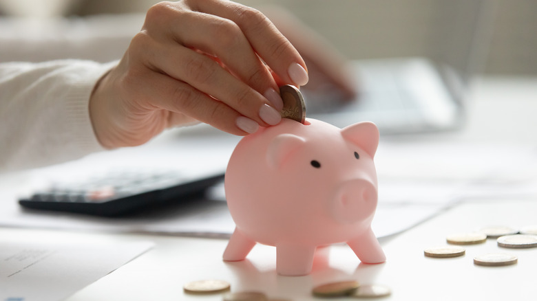 Hand putting coins into a pink piggy bank