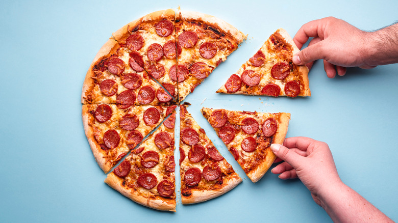 Hands grabbing slices of pepperoni pizza