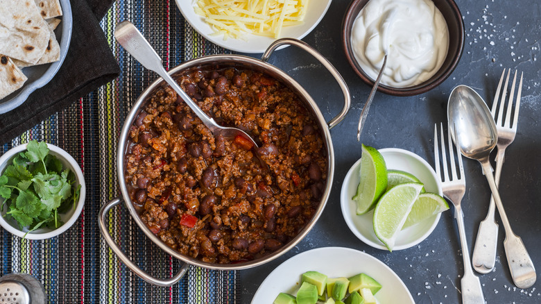 Pot of meat and bean chili surrounded by bowls of toppings