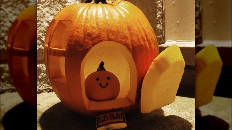 A carved pumpkin house with a mini pumpkin inside