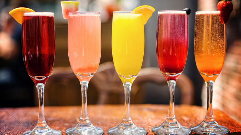 Five colorful mimosas with fruit garnishes