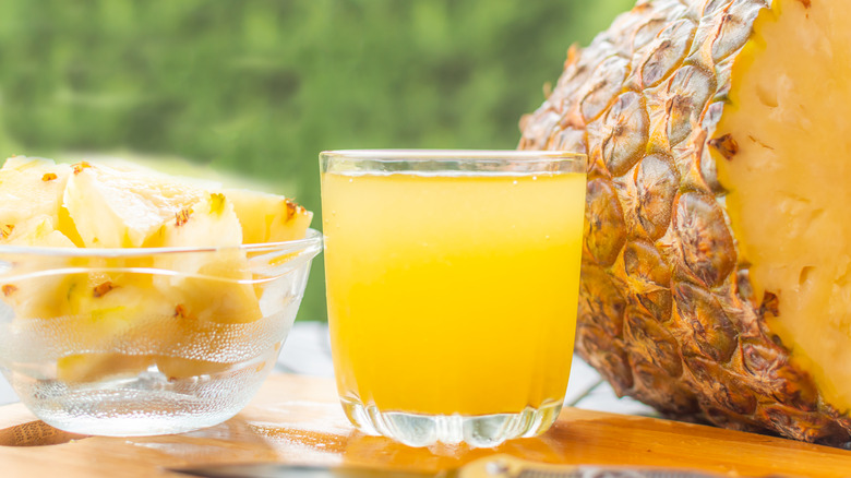 glass of pineapple juice next to pineapple chunks