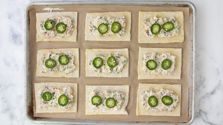 pastry rectangles with cheese mixture and jalapeño slices on baking sheet