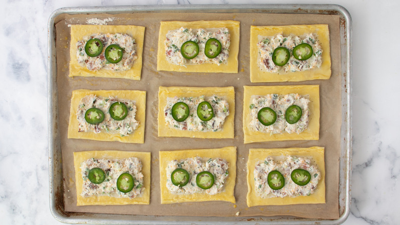 egg washed pastry rectangles with cheese mixture and jalapeño slices on baking sheet