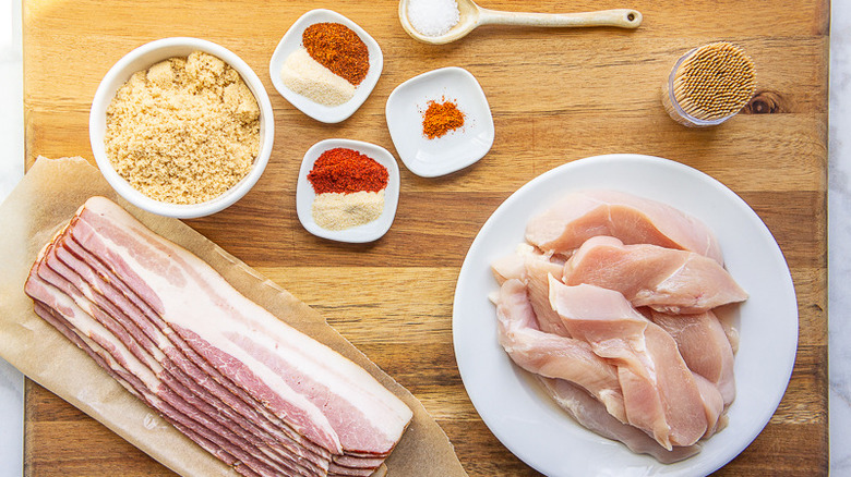 bacon, chicken tenders, spices, and brown sugar on a wooden cutting board