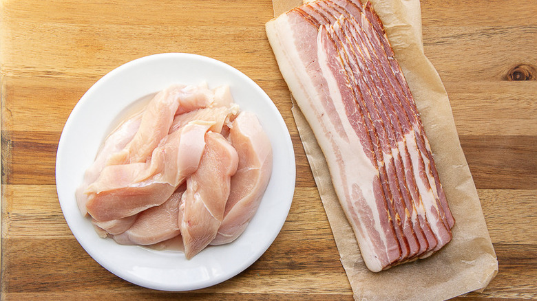 chicken tenders on a white plate with bacon on a wooden cutting board