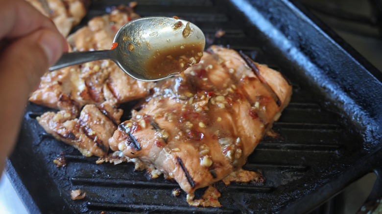 spooning marinade over grilling salmon