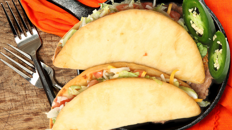 Two bean chalupas on skillet on wooden table with forks