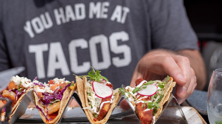 Man in "You had Me At Tacos" shirt eating tacos