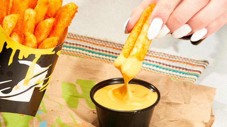 Hand dipping fries into cheese tub