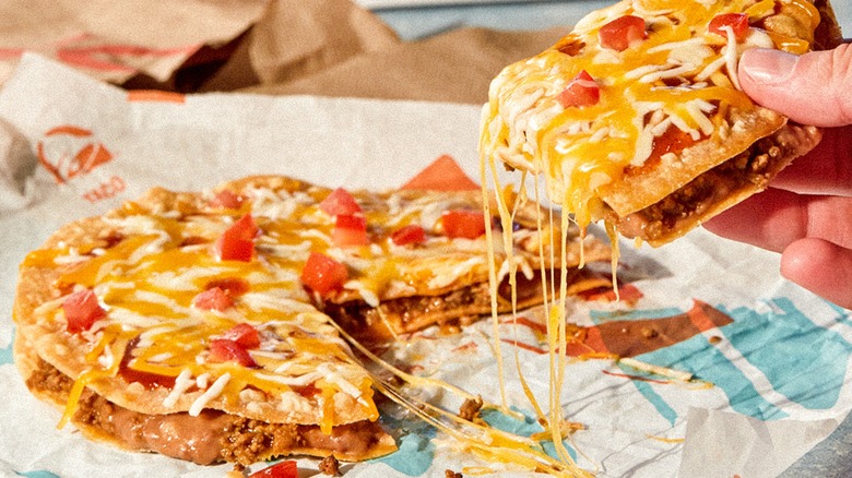 Person pulling apart slice of Mexican Pizza