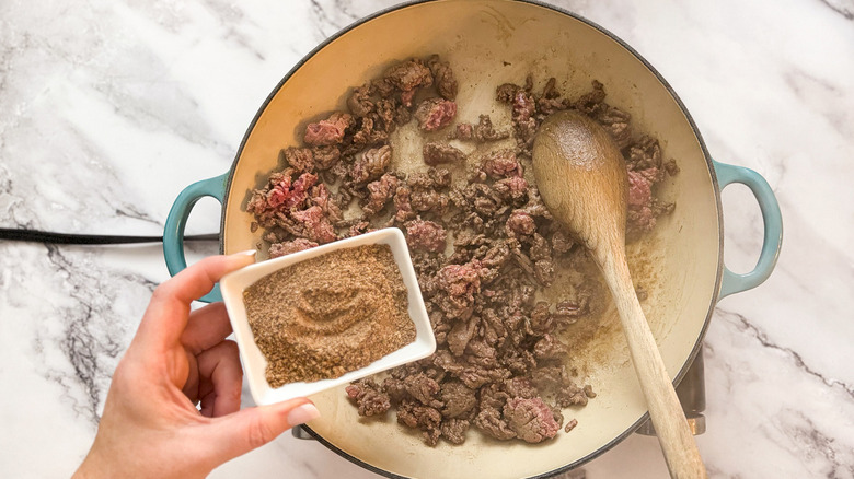 hand adding taco seasoning to beef