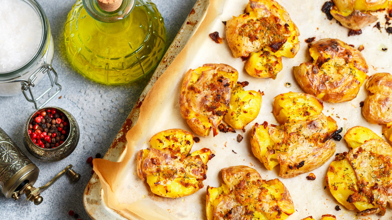 Smashed potatoes on baking sheet with seasonings and olive oil