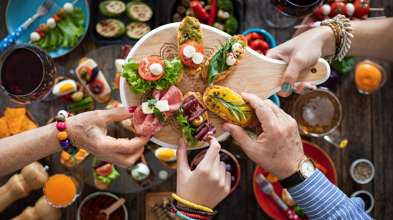 Several hands taking tapas off of a serving board