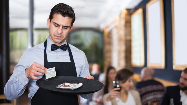 Waiter in bowtie looking at receipt