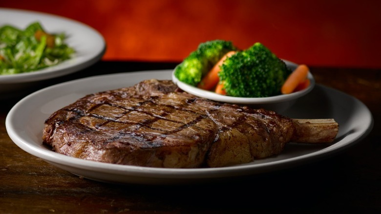 large bone-in ribeye steak next to a bowl of vegetables