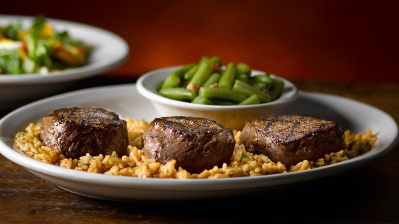 Three steaks on a bed of rice next to green beans