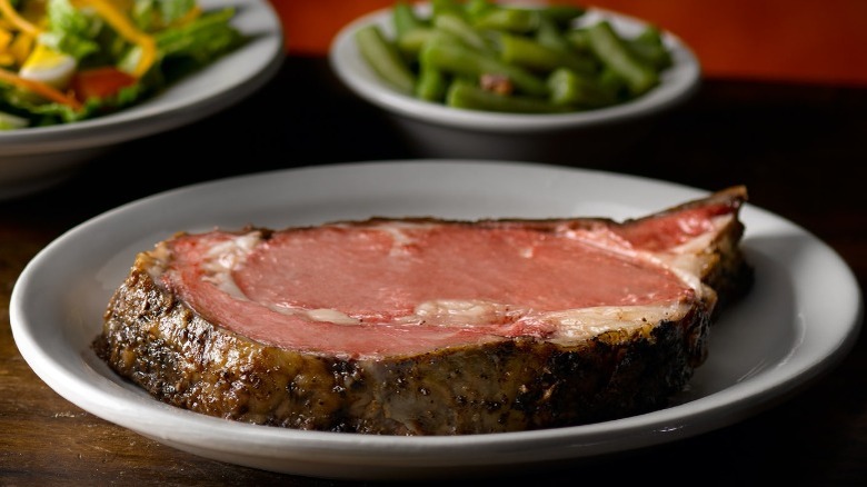 juicy prime rib on a plate with green beans and a salad