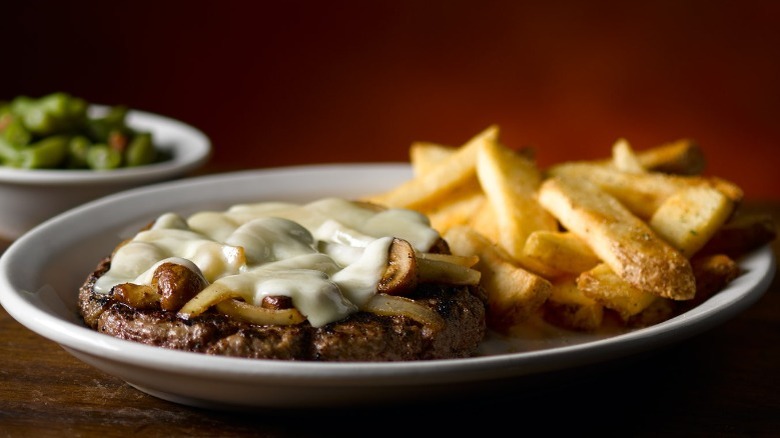 plate with steak fries and a steak covered in mushrooms, onions, and cheese