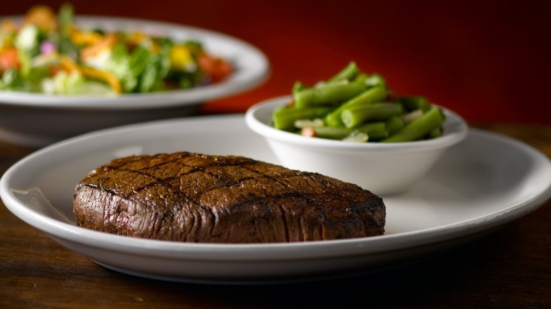 large steak next to green beans and a salad