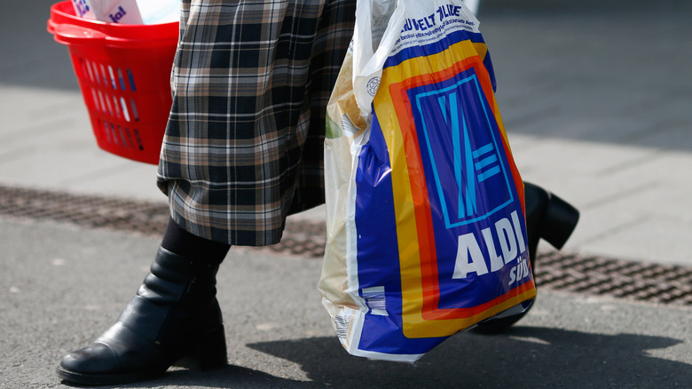 Person in plaid skirt and black boots carrying plastic Aldi bag