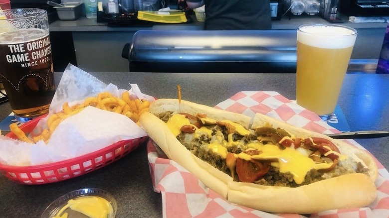 A cheesesteak, beer, and fries sit on a counter