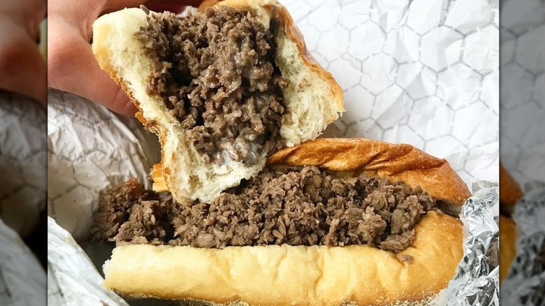 A person grabs half of a cheesesteak sandwich