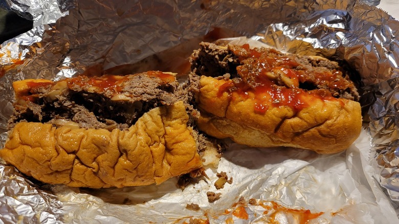 A cheesesteak cut in half has ketchup on it