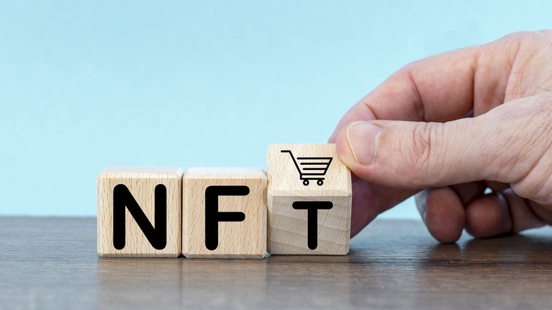 A hand spelling out "NFT" in block letters