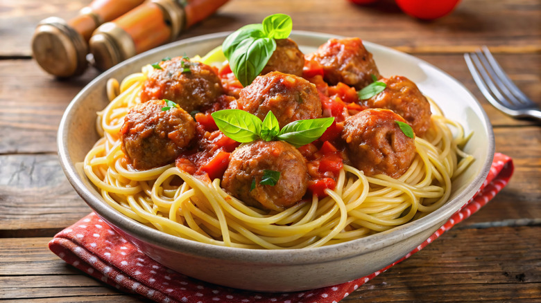 a bowl of spaghetti with tender meatballs and red sauce on a rustic wood table