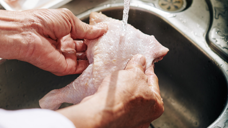 Person rinsing raw meat under faucet