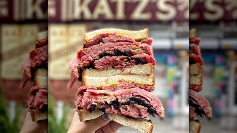 pastrami sandwich held in front of katz's sign