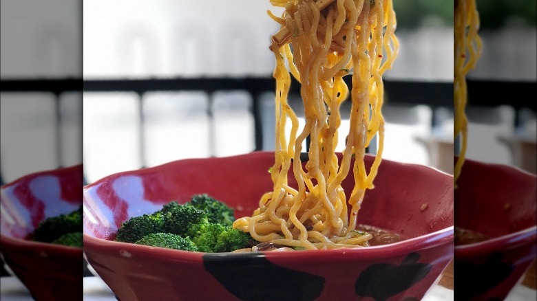 noodles cascading into red bowl with broccoli