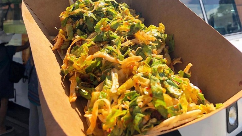 cardstock takeaway tray with Korean fusion tacos held in front of taco truck