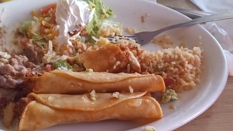 rolled tacos or flautas on plate with rice, refried beans, and additional toppings