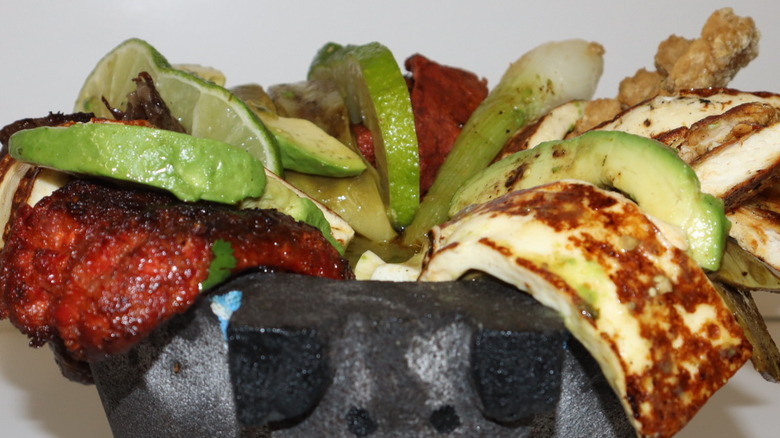 Mexican molcajete with assorted meats, lime, and avocado