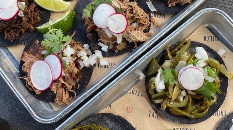 two trays of tacos with blue corn masa tortillas and various fillings