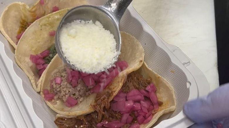 takeaway container with four chorizo tacos with scoop applying cotija