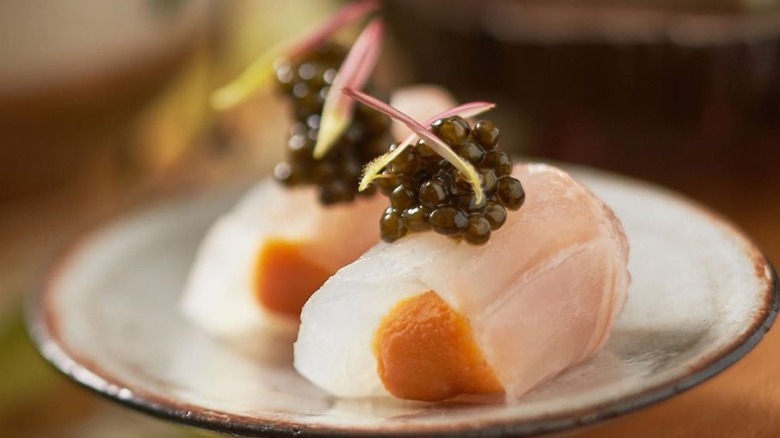 White fish topped with olive green roe on a small plate