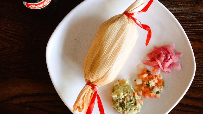 a single tamale on a white plate garnishes on the side