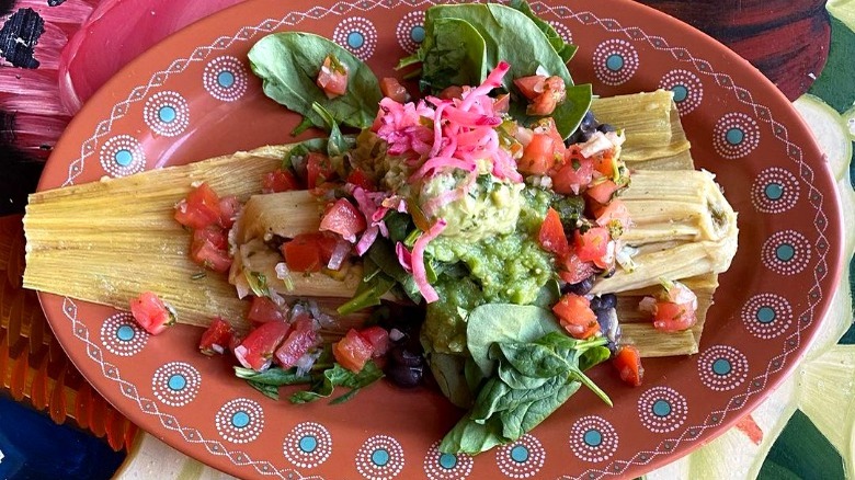 freshly garnished tamale with guacamole and pico on a red plate