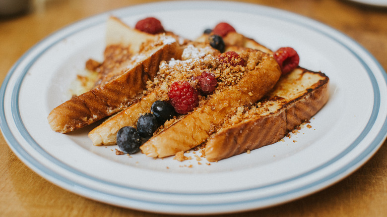 French toast on a plate with raspberries, blueberries, and a crumble topping