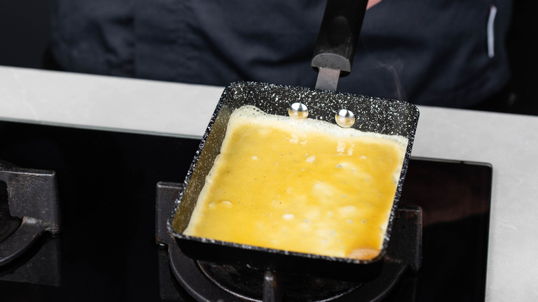 A thin omelet is being cooked in a square pan on the stove.