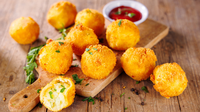 Aranchini balls are arranged on a cutting boad with a side of dipping sauce.