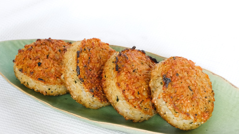 A row of four crispy grilled rice cakes is on a green plate.