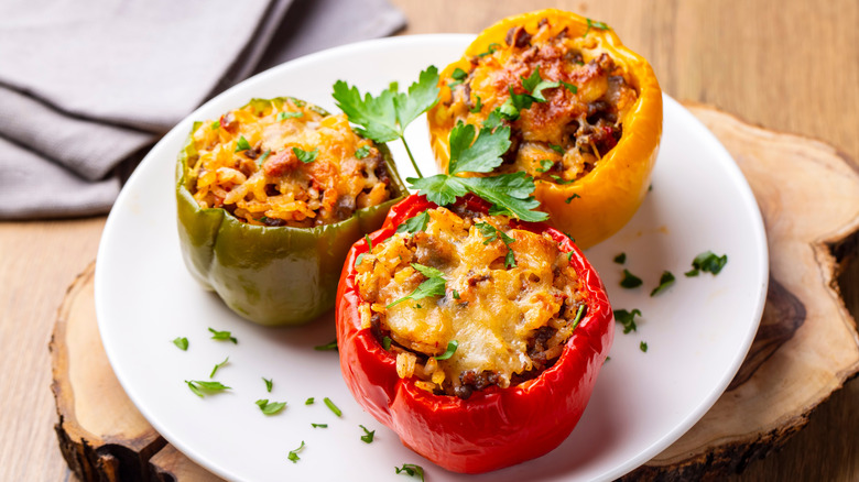 There are yellow, green, and red stuffed peppers arranged on a plate.