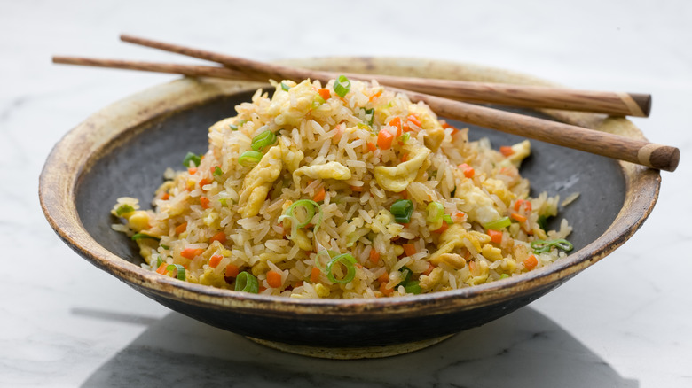 A bowl of fried rice has chopsticks on the side.