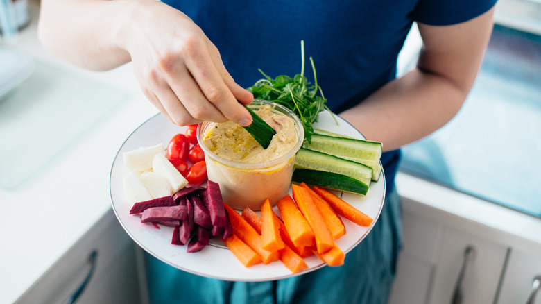 hand dipping cucumber in hummus 