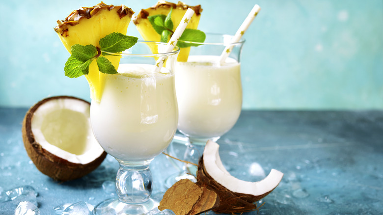 Two pina coladas garnished with pineapple and coconut