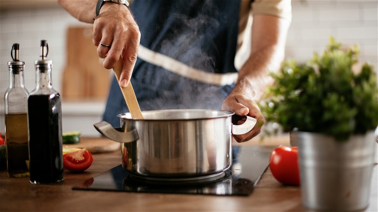 Person wearing apron stirring a pot with in a kitchen.